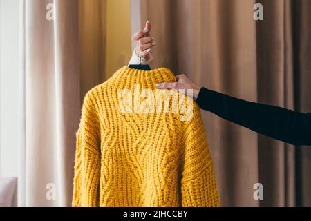 Gros plan. La main d'un vendeur ou d'un consultant passant des vêtements, un chandail jaune sur un cintre, à la main d'un client qui attend dans le f Banque D'Images