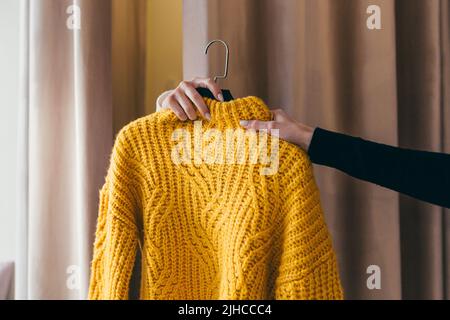 Gros plan. La main d'un vendeur ou d'un consultant passant des vêtements, un chandail jaune sur un cintre, à la main d'un client qui attend dans le f Banque D'Images