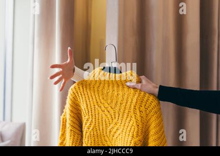 Gros plan. La main d'un vendeur ou d'un consultant passant des vêtements, un chandail jaune sur un cintre, à la main d'un client qui attend dans le f Banque D'Images