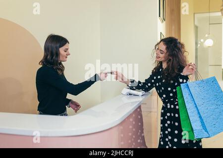 Calcul dans l'épicerie. Jeune belle femme paie par carte de crédit pour ses achats. Donne une carte de crédit au caissier. Le vendeur donne à la femme des sacs en papier avec les marchandises. Se tenir au comptoir du magasin dans le centre commercial Banque D'Images