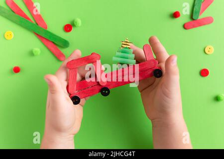 Voiture rouge avec sapin en bâtonnets de bois. Fait à la main. Projet de créativité, d'artisanat, d'artisanat pour les enfants. Mains de l'enfant Banque D'Images