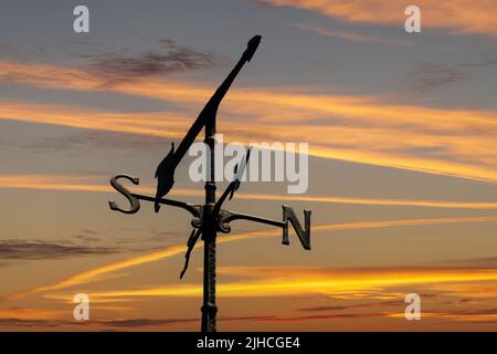 Une girouette météorologique pointe vers l'ouest avec un ciel de coucher de soleil en arrière-plan dans une image composite. Banque D'Images