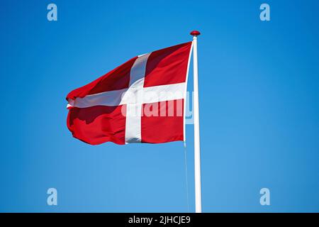 Le drapeau danois. Le drapeau danois soufflant sur fond bleu. Banque D'Images