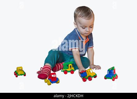 L'enfant s'assoit sur le sol et joue avec des voitures colorées. Le garçon joue avec des jouets. Isolé. Banque D'Images