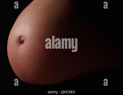 Photo détaillée d'un ventre de femme enceinte contre le noir. Ventre d'une femme enceinte sur fond noir. Banque D'Images