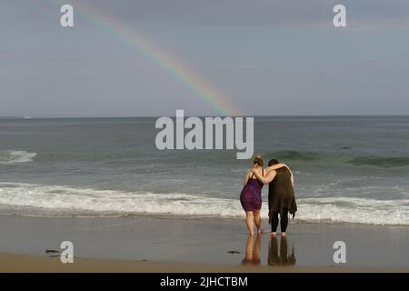 Deux femmes embrassent tout en regardant une forme arc-en-ciel sur les eaux du golfe du Maine. Banque D'Images