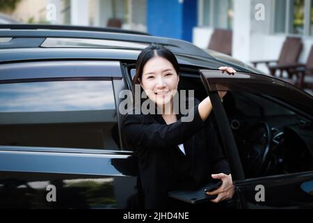 Les hommes d'affaires, les propriétaires d'entreprise, les présidents d'entreprise ou les femmes d'affaires asiatiques qui détiennent un smartphone et une tablette sortent de leur voiture pour y assister Banque D'Images
