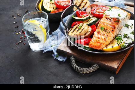 Steak de saumon avec légumes et sauce blanche sur fond sombre. Fraîchement grillé. Dîner sain. Régime méditerranéen. Banque D'Images