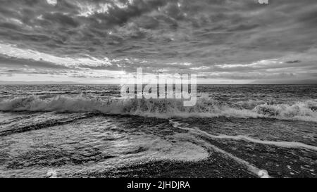 Une vague océanique se brise avec des nuages au-dessus de la tête noir et blanc Banque D'Images