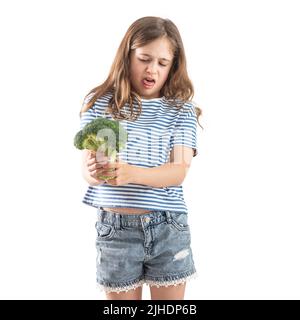 Une petite fille tient le brocoli brut dans sa main et le regarde avec distaste. Isolé sur fond blanc. Banque D'Images