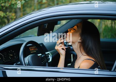 Femme élégante appliquant un rouge à lèvres en étant assise dans la voiture Banque D'Images