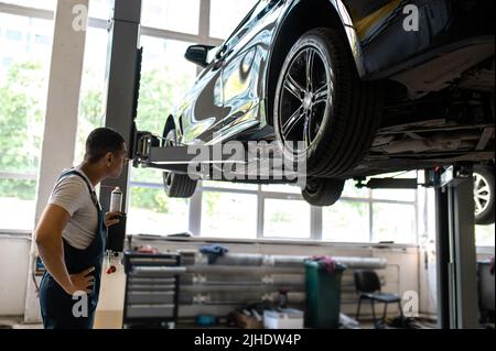 Techniciens du service après-vente de voitures effectuant le levage de voiture pour l'inspection de voiture Banque D'Images