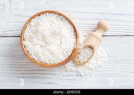 Flocons de noix de coco dans un bol en bois avec pelle sur fond de bois blanc Banque D'Images
