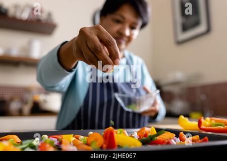 Vue à angle bas de la femme mûre biraciale garni de légumes frais salade dans la cuisine Banque D'Images