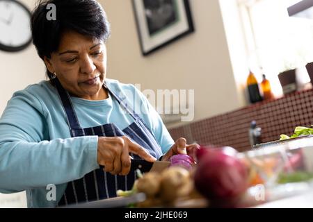 Vue à angle bas de la femme biracial mature avec les cheveux courts coupant des légumes sur l'île de cuisine Banque D'Images