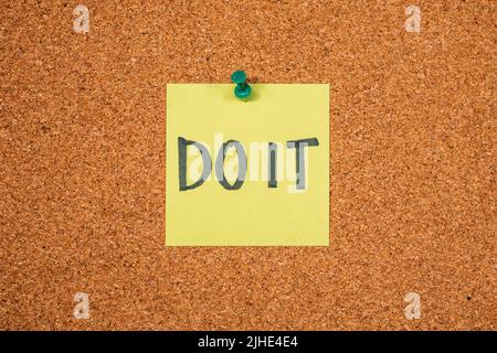 Note autocollante jaune sur un tableau en liège avec le mot « Do IT » Banque D'Images