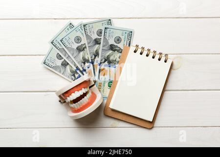 Composition de pose à plat avec modèle de typographie dentaire pédagogique et argent avec carnet sur table colorée, vue de dessus. Traitement coûteux. Banque D'Images