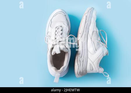 Baskets vieilles blanches sales sur fond bleu. Banque D'Images
