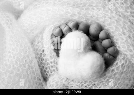 Pieds doux d'un nouveau-né dans une couverture de laine. Coeur tricoté dans les jambes de bébé. Photographie macro. Noir et blanc. Banque D'Images