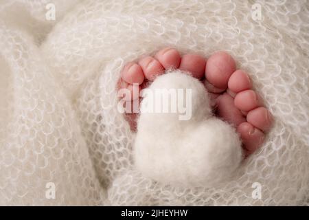 Coeur blanc tricoté dans les jambes d'un bébé. Gros plan des orteils, des talons et des pieds d'un nouveau-né. Le pied minuscule du nouveau-né. Banque D'Images