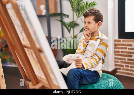 Enfant blond dessinant avec expression de doute au studio d'art Banque D'Images