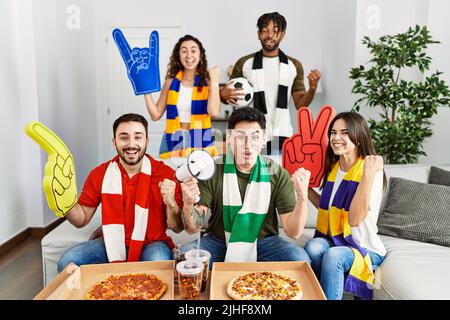 Groupe de jeunes portant le foulard d'équipe applaudissent le match de football criant fier, célébrant la victoire et le succès très excité avec les bras levés Banque D'Images