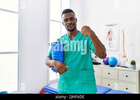 Un jeune physiothérapeute africain tenant un rouleau de mousse à la clinique pointant du doigt vers un individu souriant heureux et fier Banque D'Images