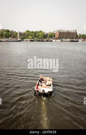 Les gens profitent du soleil dans un petit bateau à moteur sur le canal lors d'une journée chaude et ensoleillée à Amsterdam, pays-Bas. Banque D'Images