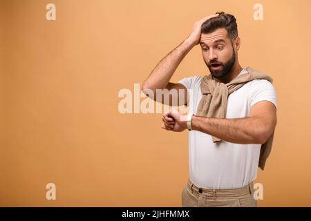 Jeune homme d'affaires beau regardant l'heure de montre inquiet, peur de se mettre tard, se tenant isolé sur fond orange, oublié de se rencontrer Banque D'Images