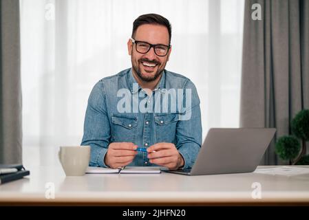 Portrait en tête d'un homme d'affaires souriant et réussi assis au bureau avec ordinateur portable. Joyeux jeune homme indépendant regardant la caméra, le travail ou s Banque D'Images
