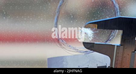 Sur la scène du crime, la police scientifique mesure le calibre du trou laissé par un impact de balle dans le verre d'une fenêtre Banque D'Images