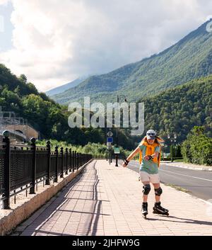 bonne jeune femme dans l'équipement de protection sur des patins à roulettes le long de remblai en été active mode de vie, activités de plein air, patinage à roulettes Banque D'Images