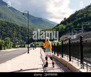 bonne jeune femme dans l'équipement de protection sur des patins à roulettes le long de remblai en été active mode de vie, activités de plein air, patinage à roulettes Banque D'Images