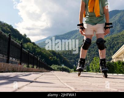 femme en équipement de protection sur patins à roulettes le long d'un remblai en été vie active, activités de plein air, patinage à roulettes sans visage Banque D'Images
