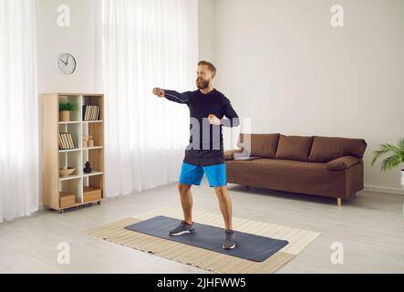 L'homme sportif fait du sport à la maison en faisant de l'entraînement cardio avec des coups intenses à l'air. Banque D'Images