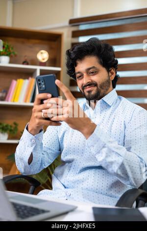 Happy Young, employé d'entreprise occupé à utiliser le téléphone mobile au bureau, devant l'ordinateur portable au bureau - concept de détente, de pause et de médias sociaux Banque D'Images