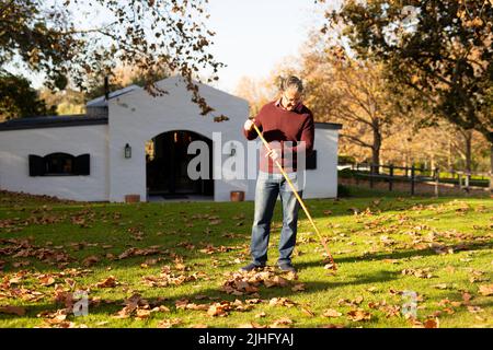 Image d'un homme âgé caucasien heureux qui balaie les feuilles dans le jardin Banque D'Images