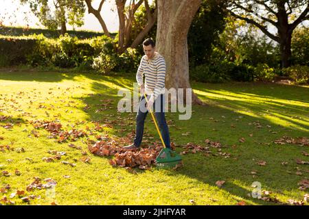 Image d'un homme caucasien heureux qui balaie les feuilles dans le jardin Banque D'Images