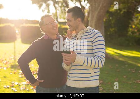 Image d'un père caucasien heureux et d'un fils adulte prenant le selfie dans le jardin Banque D'Images