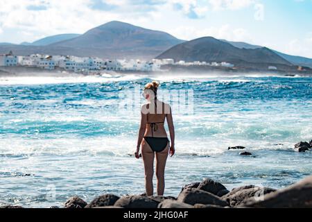 Femme touriste à la plage sauvage rocheuse et le littoral de surf spot la Santa Lanzarote, îles Canaries, Espagne. Village de la Santa et volcan de la montagne Banque D'Images