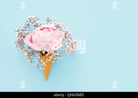 Pivoine rose et gitsophila dans un cône de glace gaufré sur fond bleu. Fête des mères, Saint Valentin, Bachelorette, concept d'été. Copier l'espace Banque D'Images