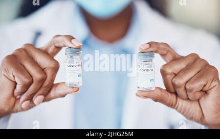 Gros plan de femme afro-américaine médecin tenant deux bouteilles du vaccin contre le virus corona tout en se tenant dans son bureau d'hôpital. Soyez sûr pendant Banque D'Images
