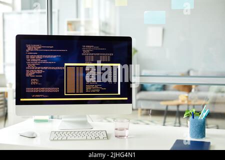 Gros plan du lieu de travail du programmeur avec ordinateur debout sur lui avec des codes sur moniteur au bureau Banque D'Images