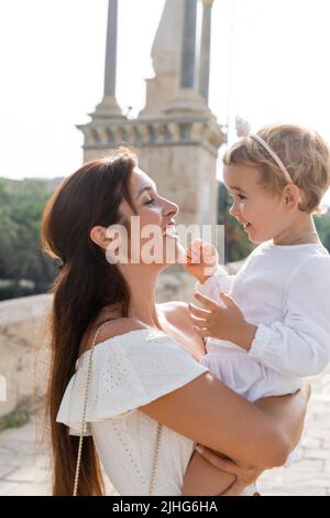 Vue latérale d'une maman brune heureuse qui embrasse sa petite fille à Valence Banque D'Images