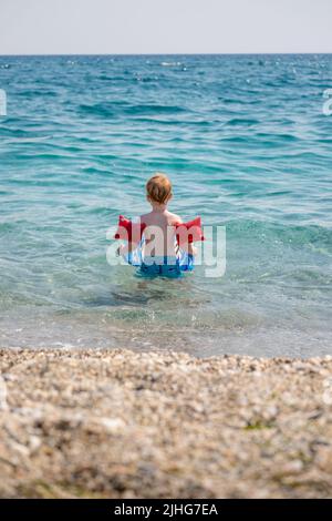 Adorable petit garçon jouant et nageant avec ses brassards gonflables une planche de natation dans la mer Banque D'Images