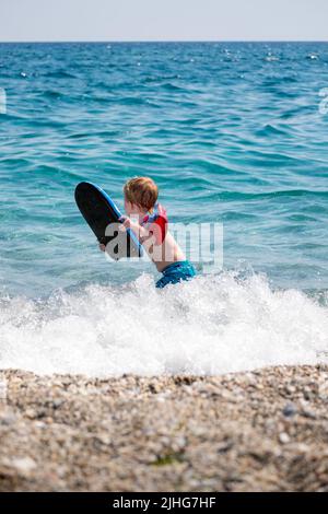 Adorable petit garçon jouant et nageant avec ses brassards gonflables une planche de natation dans la mer Banque D'Images