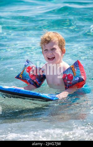 Adorable petit garçon jouant et nageant avec ses brassards gonflables une planche de natation dans la mer Banque D'Images