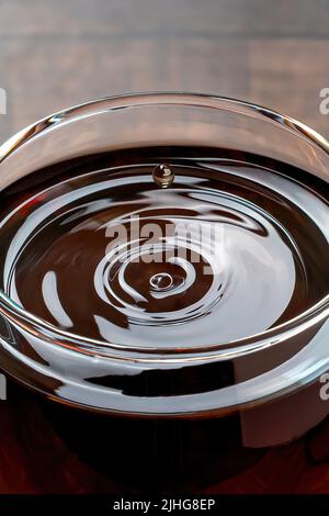 Des gouttes de vin et des vagues se forment dans un verre de vin rouge sur une table en bois Banque D'Images