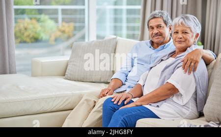Portrait d'un couple senior de race mixte affectueux se détendant dans leur salon à la maison. Homme hispanique et femme se liant sur le canapé dans la vie Banque D'Images