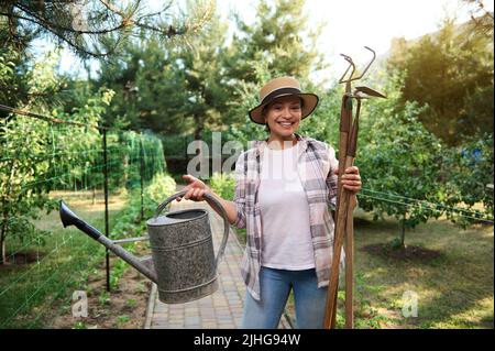 Agréable femme jardinier, fermier tient des outils de jardinage dans ses mains, aime le jardinage dans le jardin de légumes biologiques Banque D'Images